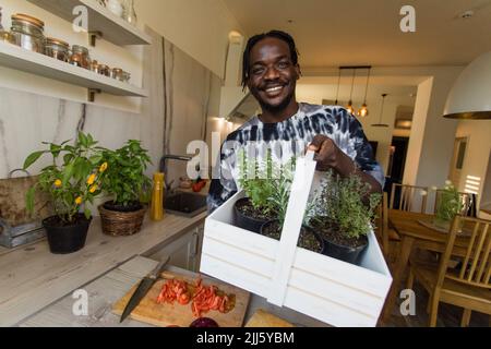 Uomo sorridente che tiene un cesto con rosmarino e piante di timo a casa Foto Stock