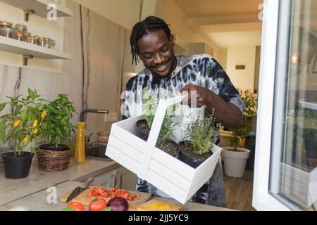 Uomo sorridente che tiene un cesto con rosmarino e piante di timo a casa Foto Stock