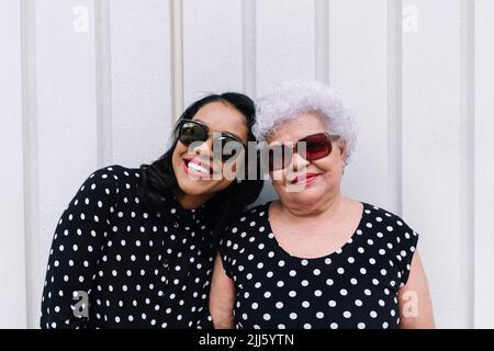 Felice figlia e madre indossare occhiali da sole di fronte alla parete bianca Foto Stock