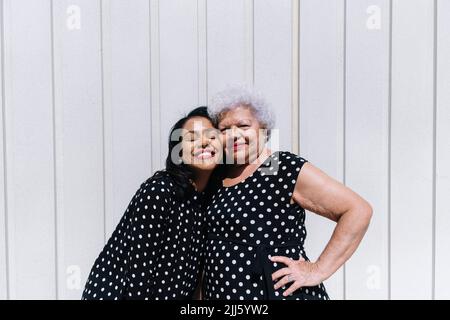 Madre e figlia in piedi guancia a guancia di fronte al muro Foto Stock