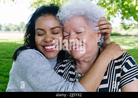 Donna felice che abbraccia la madre anziana nel parco Foto Stock