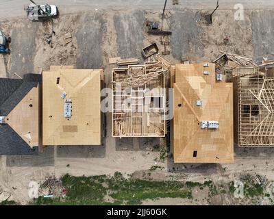 Una vista aerea sopra una fila di nuove case in costruzione. Installazione di strutture in legno e tetti vista in corso direttamente dall'alto. Foto Stock