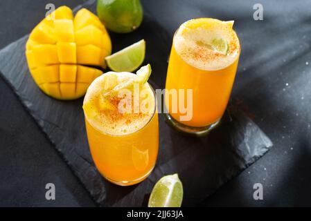 Frappè di mango messicano Mangonada con salsa di camoy e condimento al peperoncino lime e paglia di caramelle tamarindo. Due cocktail estivi Mangonada al buio Foto Stock