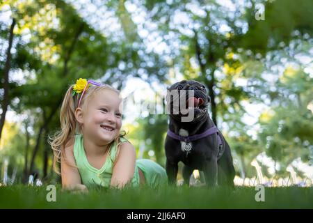 la ragazza allegra si trova sul prato del parco e guarda il bulldog francese che è accanto a lei Foto Stock