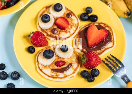 Frittelle americane decorate come sorriso e facce felici con fragole, cioccolato, mirtilli e banana. Cibo per bambini, divertente e creativo. Foto Stock