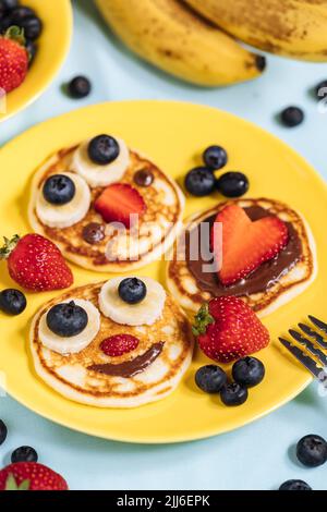 Frittelle americane decorate come sorriso e facce felici con fragole, cioccolato, mirtilli e banana. Cibo per bambini, divertente e creativo. Foto Stock