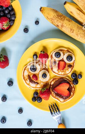 Frittelle americane decorate come sorriso e facce felici con fragole, cioccolato, mirtilli e banana. Cibo per bambini, divertente e creativo. Foto Stock