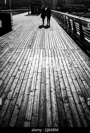 Un'immagine verticale in scala di grigi di persone che camminano sulla banchina di legno Foto Stock