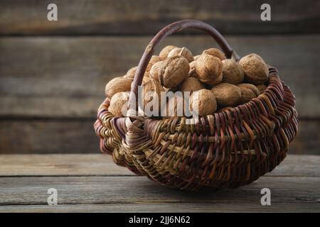 Cestino di vimini pieno di noci su tavola di legno. Foto Stock