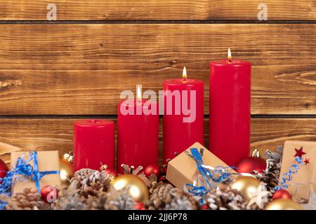 Quattro candele rosse con decorazioni natalizie con parete in legno sullo sfondo Foto Stock