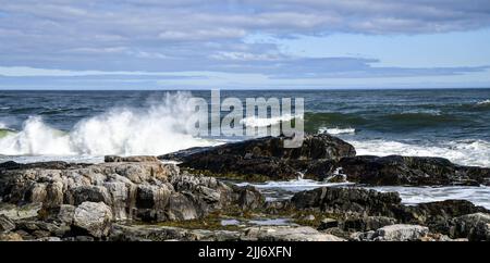 vista panoramica delle onde che si infrangono contro le rocce sotto il cielo blu e le nuvole Foto Stock