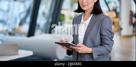 Sorridente giovane donna d'affari asiatica leader che tiene il tablet digitale in ufficio. Foto Stock