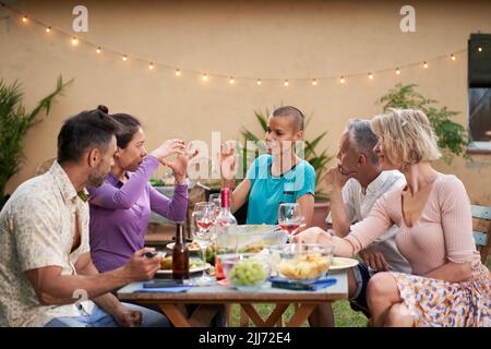 Gruppo di amici che chiacchierano durante il pranzo nel cortile. Persone di mezza età che hanno una discussione all'aperto a tavola mentre mangiano e bevono Foto Stock