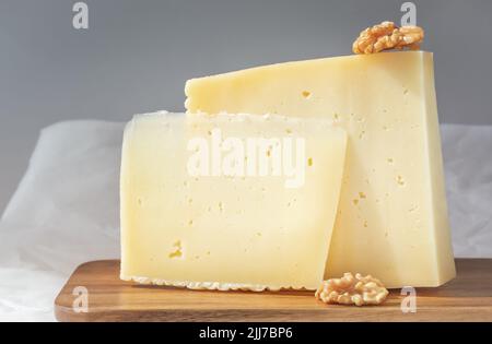 Coppia di pezzi di formaggio duro con noci su sfondo grigio Foto Stock