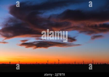 Silhouette di una serie di moderni mulini a vento sotto un tramonto rossastro, con un cielo con alcune nuvole, alla periferia di Kiyú, San José, Uruguay Foto Stock