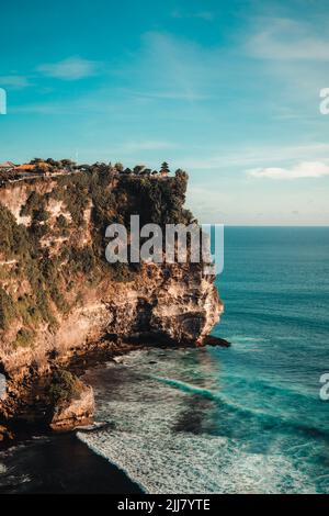 Le onde morbide dell'oceano con schiuma sulle rocce dall'enorme scogliera del tempio di Uluwatu a Bali, Indonesia Foto Stock