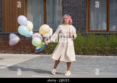 Donna in capelli colorati cammina con un'armatura di palloncini e beve una bevanda rinfrescante Foto Stock