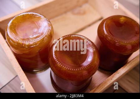 Vista dall'alto della marmellata di albicocche fatta in casa con i box e pezzi di pesche in scatola in vasetti di vetro capovolti su una cassa di legno. Copiare lo spazio dell'annuncio. Tradizionale re Foto Stock