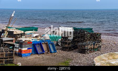 Attrezzatura da pesca immagazzinata sulla spiaggia di pietra a Budleigh Salton in Devon. Pentole, reti, vassoi, barche, aste, corda conservata in modo ordinato ogni giorno. Foto Stock