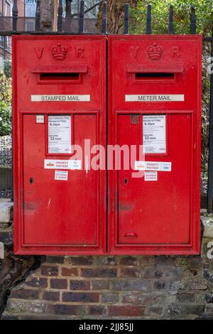 Un paio di iconiche scatole rosse vittoriane dell'ufficio postale Royal Mail affisse sulle ringhiere della città di Londra ancora in uso oggi Foto Stock