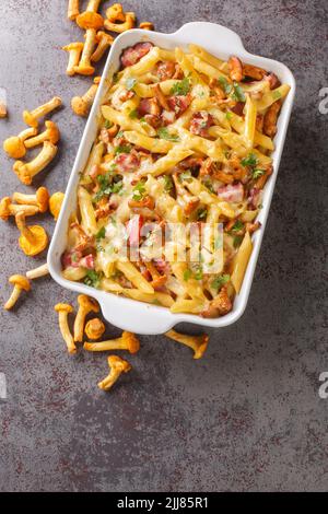 Gratin preparato da pasta penne con funghi di chanterelle, carne e formaggio da vicino in una teglia in ceramica sul tavolo. Vista dall'alto verticale da ab Foto Stock