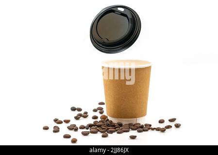 Tazza di caffè calda in carta marrone con chicchi di caffè sul pavimento, coperchio della tazza in plastica che galleggia nell'aria, caffè caldo in carta marrone isolato Foto Stock