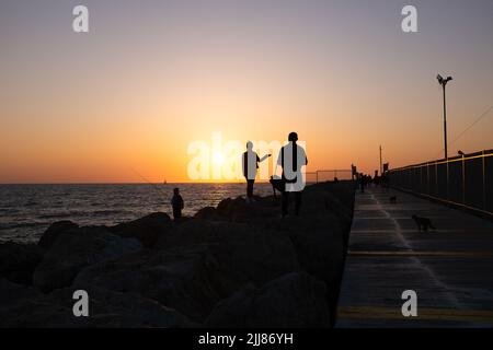 Silhouette di persone su un molo di mare durante il tramonto. Foto Stock