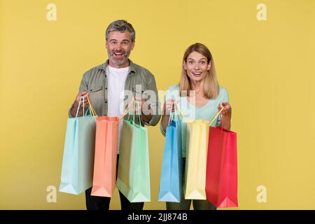 Grande vendita e shopping con piacere. Sposi eccitati di mezza età che tengono molti pacchetti colorati nelle mani Foto Stock