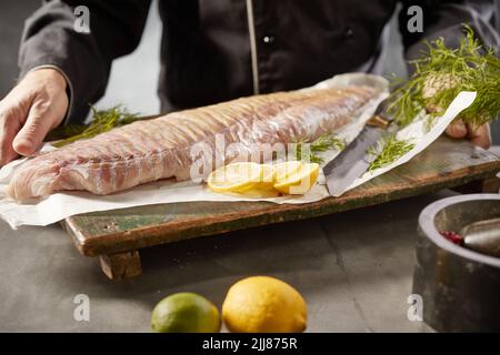 Raccolto anonimo chef maschio in piedi con filetto di pesce crudo sul tagliere in cucina Foto Stock