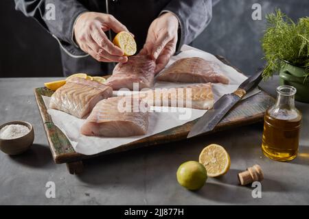 Da sopra di raccolto anonimo maschio cuoco aggiungere succo di limone su filetto di pesce crudo mentre preparare gustoso piatto in cucina Foto Stock