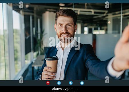 Videoconferenza. Un uomo d'affari positivo che fa una chiamata virtuale e beve caffè, sorridendo alla fotocamera, screenshot pov Foto Stock