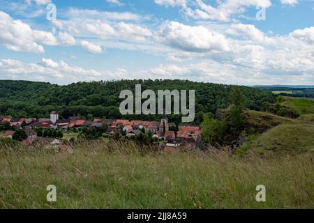 Rechts unten ist eine kleine Felsformation zu sehen , im tal ein Ort , umgeben von Wald u Wiesen. Ein blauer Himmel mit weißen Wolken liegt über der Sz Foto Stock