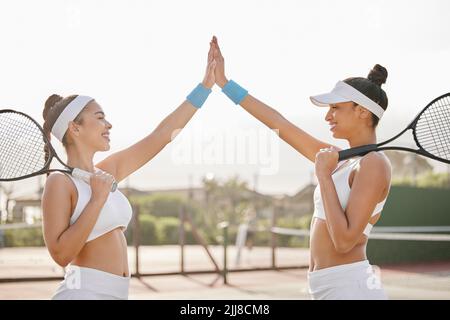Heres al lavoro di squadra e il campionato. Due giovani giocatori di tennis si levano in piedi insieme sul campo e si danno un alto cinque dopo la pratica. Foto Stock