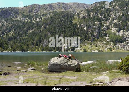 una ragazza che riposa su una roccia vicino ad un lago in montagna Foto Stock