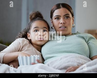 Prepararla per la terapia futura. Una madre e una figlia mangiano popcorn mentre guardano la televisione insieme a casa. Foto Stock