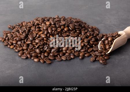 Chicchi di caffè nero arrosto con un cucchiaio di legno che si versa sul tavolo grigio. Foto Stock