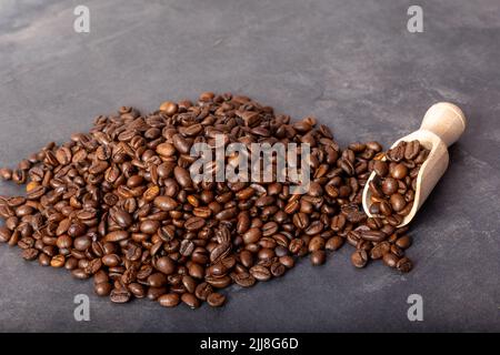 Chicchi di caffè nero arrosto con un cucchiaio di legno che si versa sul tavolo grigio. Foto Stock