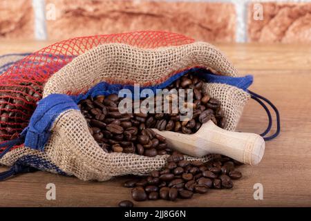 Chicchi di caffè nero arrostiti con un cucchiaio di legno, fuoriuscite dal sacco sul tavolo. Foto per una caffetteria, un caffè o un ristorante. Foto Stock