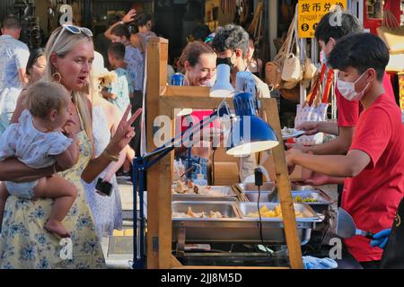 Un turista occidentale si gesticola in una bancarella di snack nel mercato di strada pedonale Domenica, Thalang Road, nella zona della Città Vecchia di Phuket, Phuket, Thailandia Foto Stock