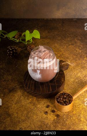 bevanda al cioccolato con ghiaccio in bicchiere e caldo in tazza, su vassoio rustico in legno e sfondo autentico Foto Stock