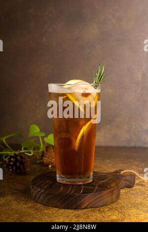 tè al limone fresco preparato con ghiaccio in vetro con fetta di limone e rosmarino, su un vassoio rustico in legno e sfondo autentico Foto Stock