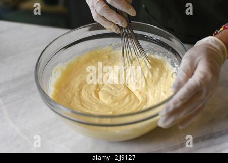 Mani in guanti di gomma mescolando l'impasto per una torta Foto Stock