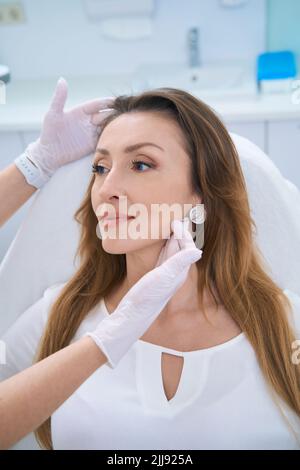 Medico femminile che esamina il viso della signora con entrambe le mani guantate Foto Stock