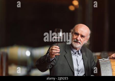 Uomo caucasico anziano di razza grigiastro degusta vino bianco in una cantina Foto Stock