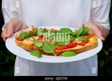 Deliziosa bruschetta italiana con mozzarella, aglio, olio d'oliva e foglie di basilico su un piatto Foto Stock