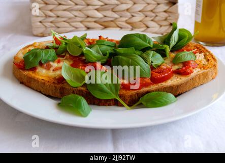 Deliziosa bruschetta italiana con mozzarella, aglio, olio d'oliva e foglie di basilico su un piatto Foto Stock