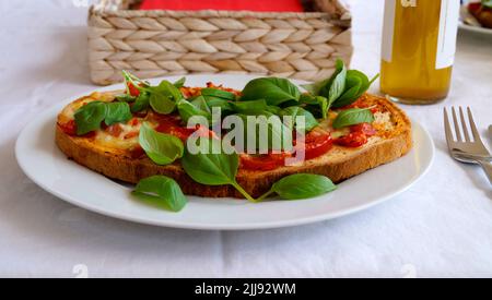 Deliziosa bruschetta italiana con mozzarella, aglio, olio d'oliva e foglie di basilico su un piatto Foto Stock