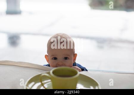 Curioso bambino toddler vuole fare male e sta guardando fino a letto dei genitori per caffè caldo tazza, astratto copia sfondo spazio Foto Stock