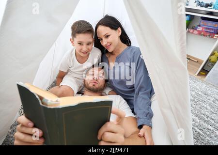 La famiglia legge una favola sera in un rifugio accogliente e magico Foto Stock