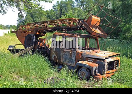 Un camion noleggiato sul lato della strada in erba verde. Un'auto bruciata e bruciata in guerra. Vittime civili e vittime. Macchina tecnica Foto Stock